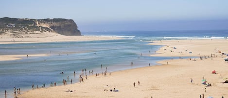 Una playa con tiendas de campaña y sombrillas, una orilla arenosa y un acantilado al fondo.