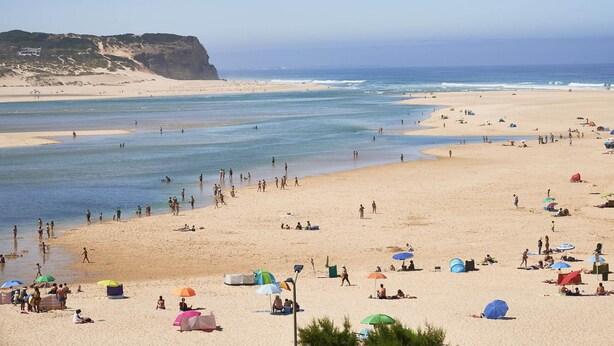 Una playa con tiendas de campaña y sombrillas, una orilla arenosa y un acantilado al fondo.