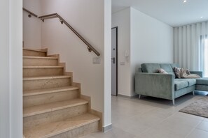 A staircase with a handrail, a light-colored wall, and a teal sofa in a modern living area. - Villa Foz - Holiday Villa with Private Pool By SCH (Foz do Arelho)