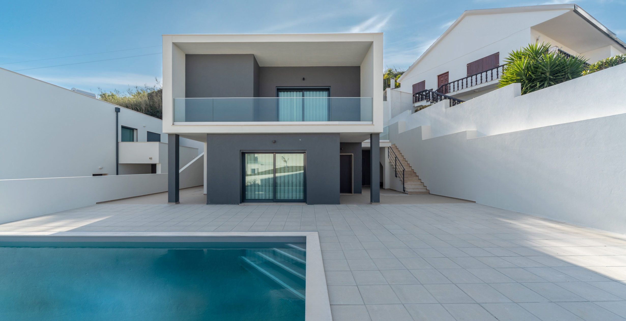 Una casa moderna de dos pisos con piscina, un balcón y una escalera que lleva al piso superior.