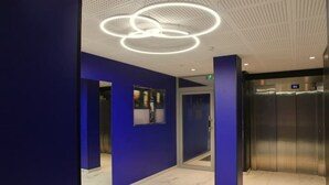 A modern elevator with a digital display, a blue wall with a circular light fixture, and a tiled floor. - A haven of peace in the heart of the city (Reims)