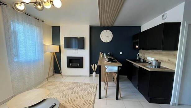 A modern kitchen with a built-in oven, a dining area with a round table and chairs, and a living space with a sofa and a lamp. - A haven of peace in the heart of the city (Reims)