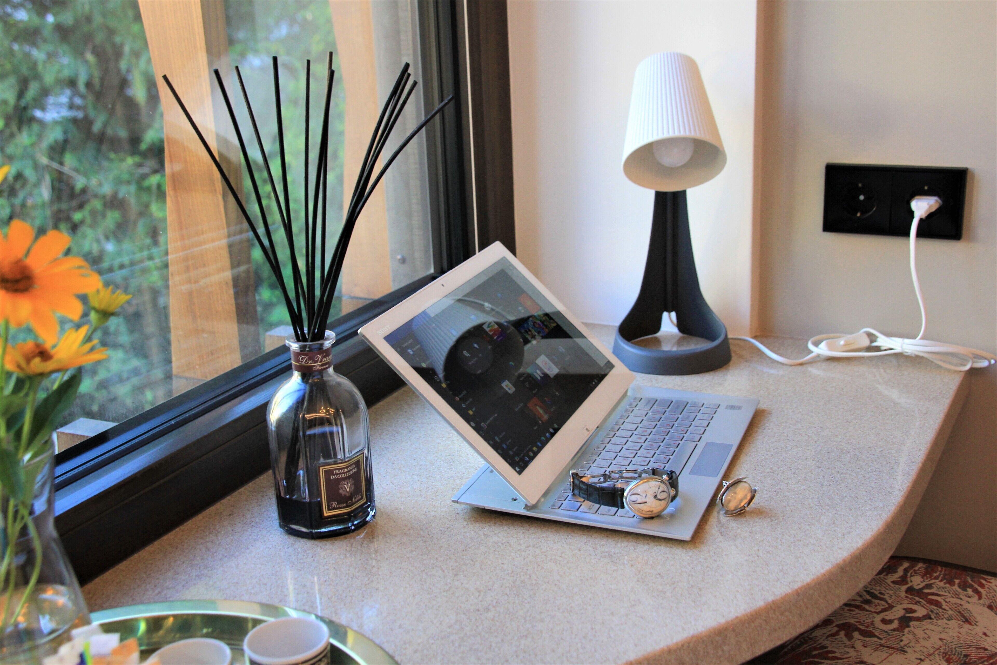 A laptop on a desk with a lamp, a bottle of perfume, and a pair of glasses.