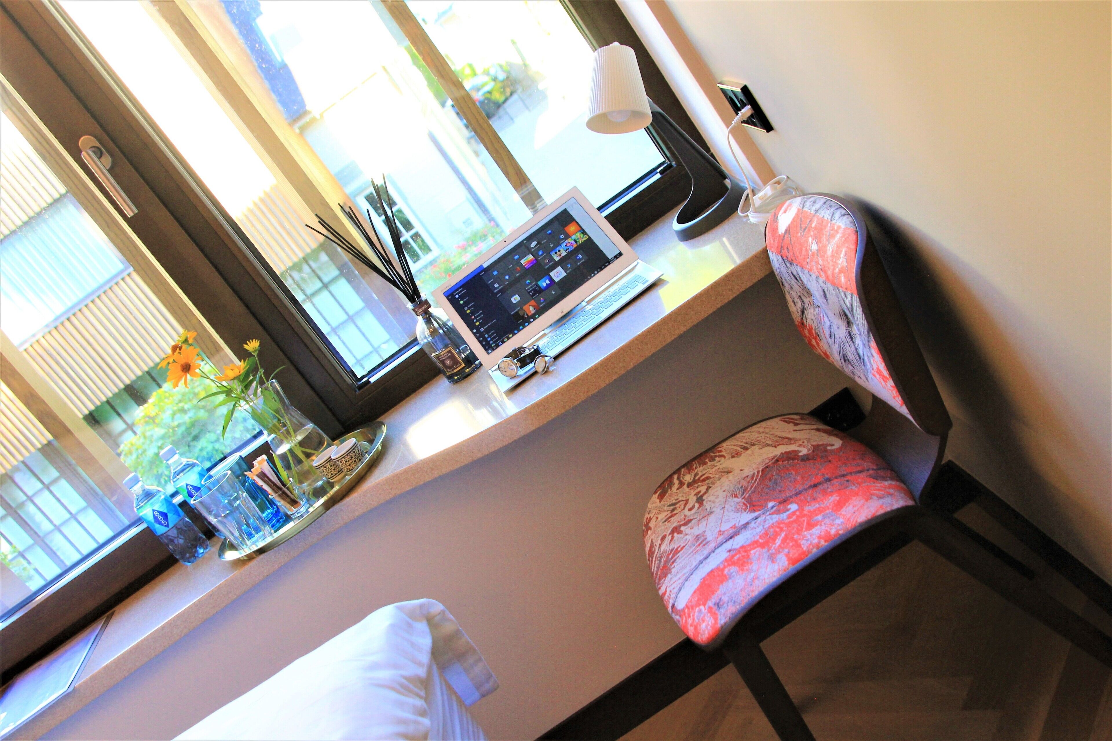 A hotel room with a desk, laptop, chair, and a window with blinds.