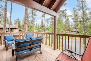 A wooden deck with wicker furniture and a view of a forested area.