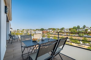 A balcony with a table and chairs, overlooking a river and a town.
