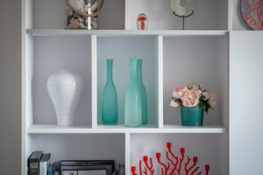 Una estantería blanca con diversos objetos decorativos, como jarrones, una escultura y un cuadro enmarcado.