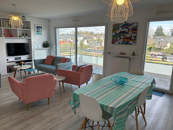 A modern living room with a TV, sofas, a dining table, and a balcony with a view.