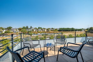 Un balcón con mobiliario exterior, una mesa y sillas, con vistas a una zona residencial con casas y vegetación.