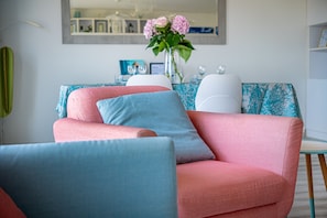 A modern living room with a sofa and armchairs, a dining table with chairs, and a vase with flowers.
