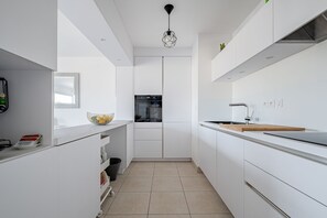 A modern kitchen with white cabinetry, a built-in oven, and a stainless steel sink.