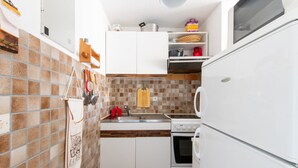 Una cocina compacta con armarios blancos, un salpicadero de azulejos y un refrigerador blanco.