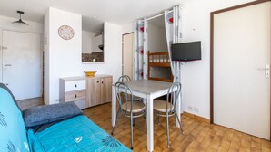 Habitación pequeña con cama, una mesita y sillas, televisor montado en la pared, un reloj y una puerta.