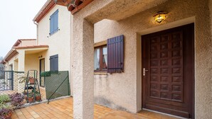 Una casa con patio de tejas, puerta de madera y ventana con contraventanas.