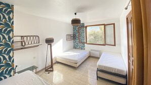 Una habitación con dos camas, una lámpara de pie, una ventana y una cortina estampada.