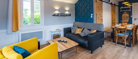 A modern living room with a sofa, yellow armchair, and a dining area with a table and chairs.