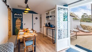 Zona pranzo con tavolo e sedie in legno, angolo cottura con pensili e macchina per il caffè, e vista su un giardino con poltrone relax.