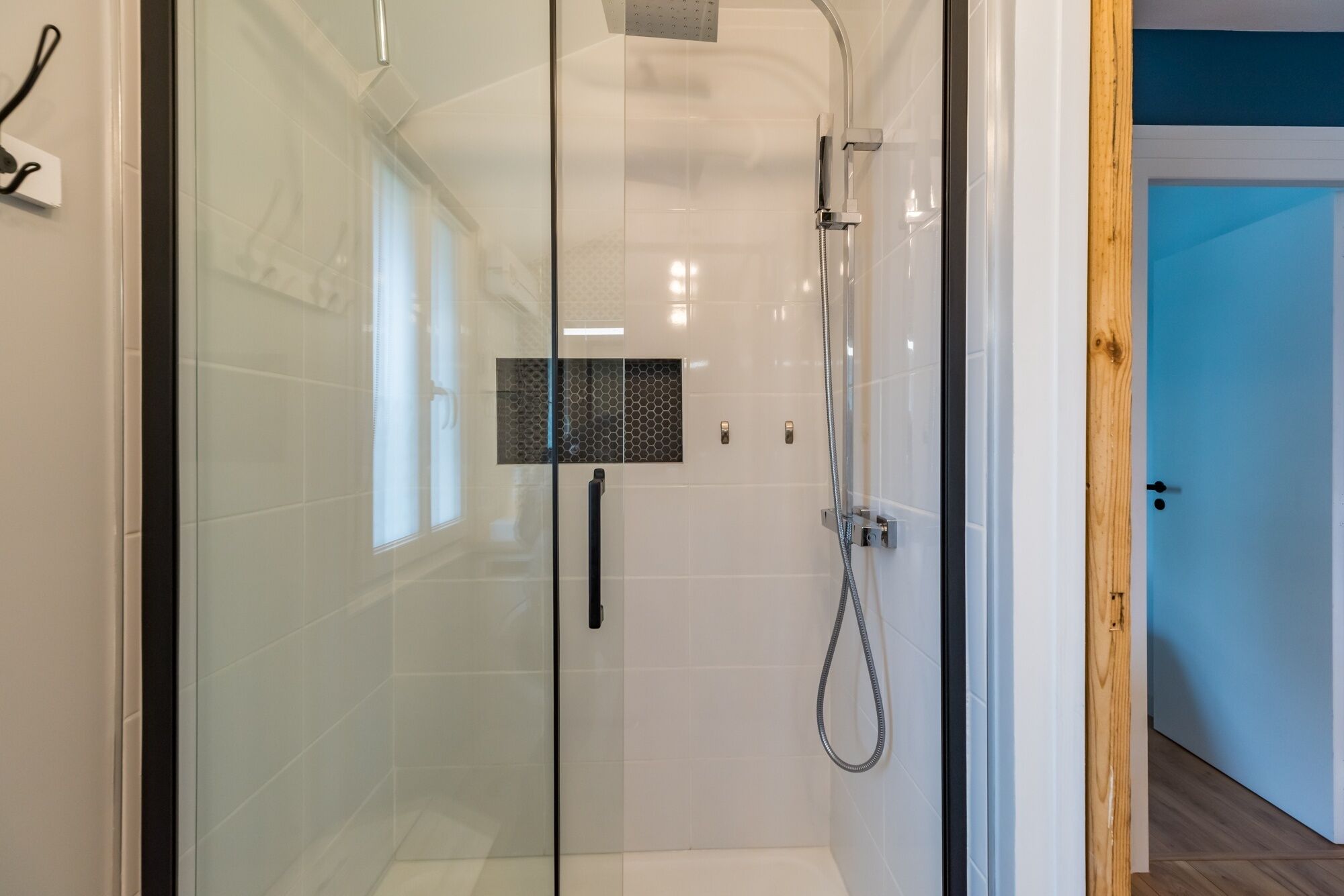 Une douche moderne dotée d’une paroi en verre, d’un pommeau de douche à main et d’un panneau de commande fixé au mur.