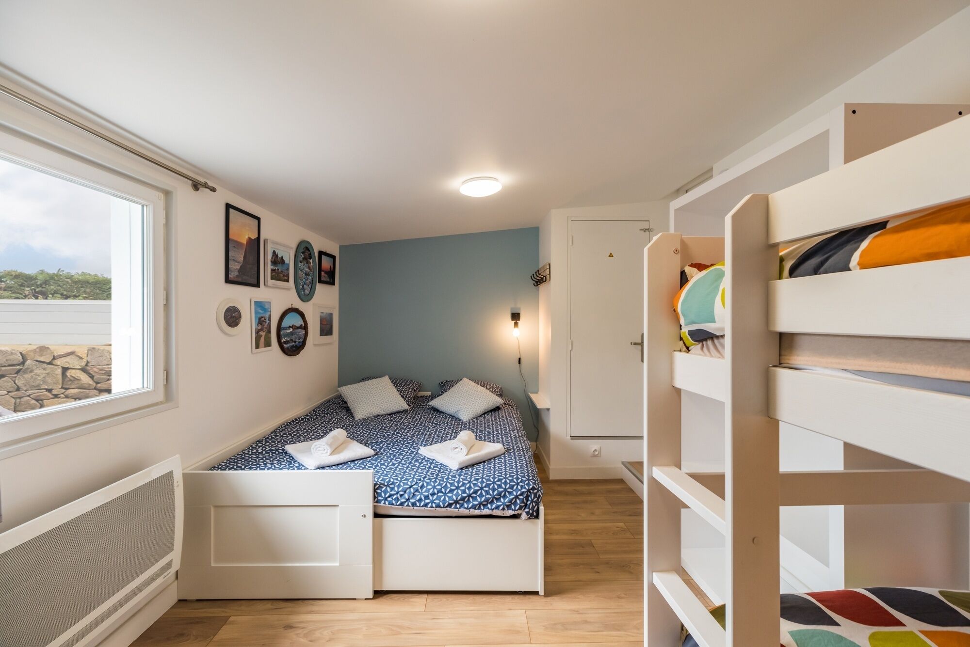 Une chambre à coucher avec un lit, des lits superposés, une fenêtre et un mur décoré de tableaux.