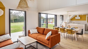 Un salon moderne comprenant un canapé, une table à manger et des chaises. Il y a également un coin cuisine avec un évier et une fenêtre donnant sur un jardin.