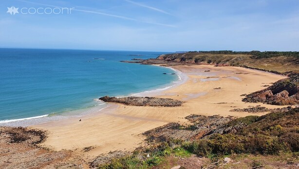 Un paysage côtier avec une plage de sable, des affleurements rocheux et un ciel bleu dégagé.
