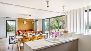 Une cuisine moderne dotée d’un grand îlot central, d’un coin repas avec des chaises jaunes et d’une vue sur l’extérieur.