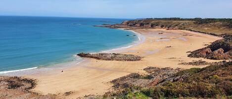 A coastal landscape with a sandy beach, rocky outcrops, and a clear blue sky.