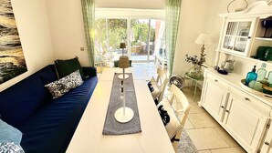 A room with a sofa, a dining table, and a cabinet. There is a view of the outdoors through a glass door. - La Pélagie - Maison 6 personnes (Sainte-Maxime)