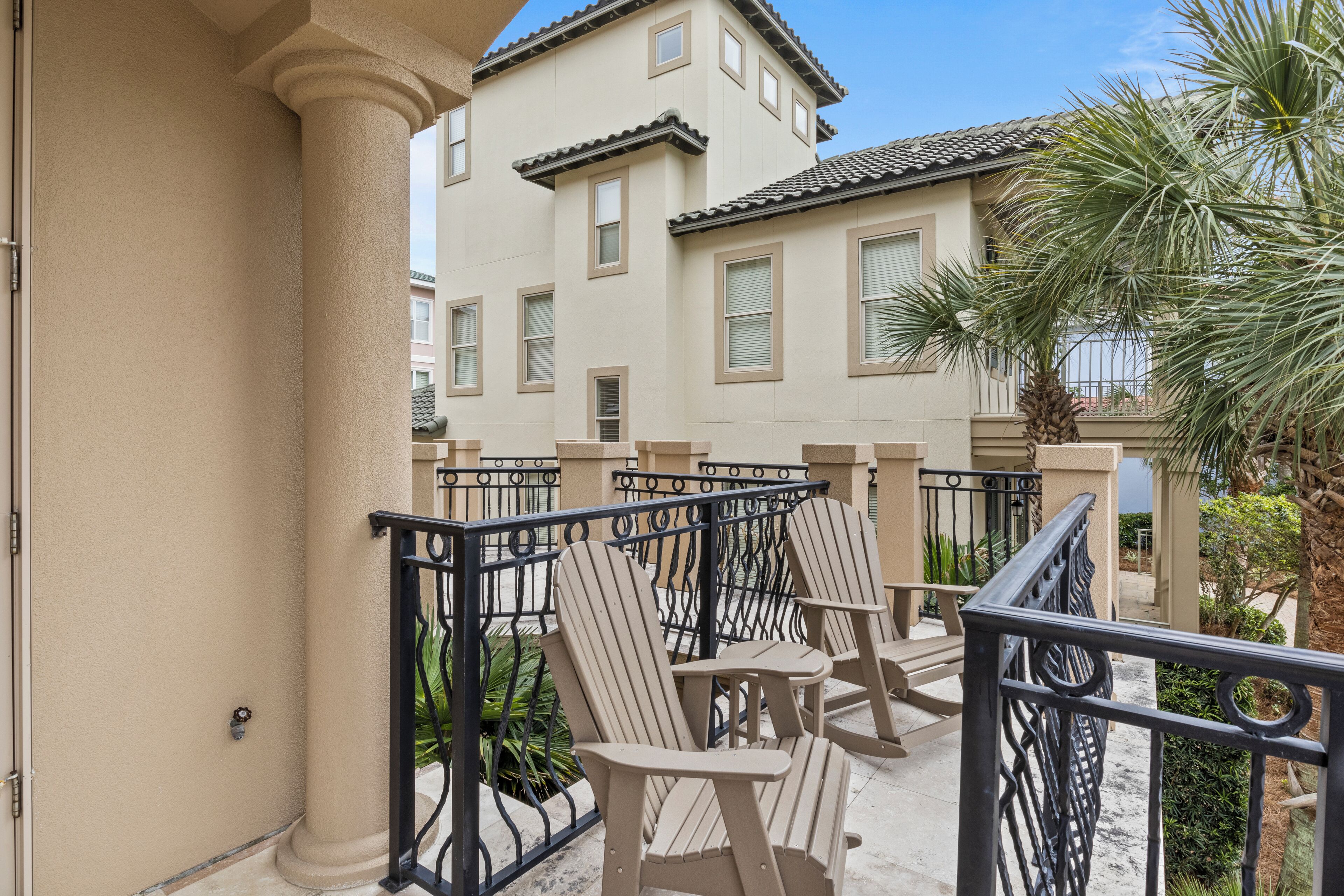 A balcony with beige chairs and a black railing, overlooking a building with a tiled roof and windows.