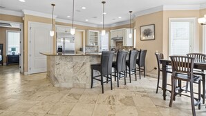 Una cocina amplia con una isla de mármol, taburetes de bar, iluminación colgante y un comedor con mesa y sillas.