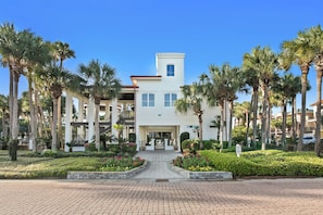 A hotel with a central entrance, surrounded by palm trees and well-maintained gardens.