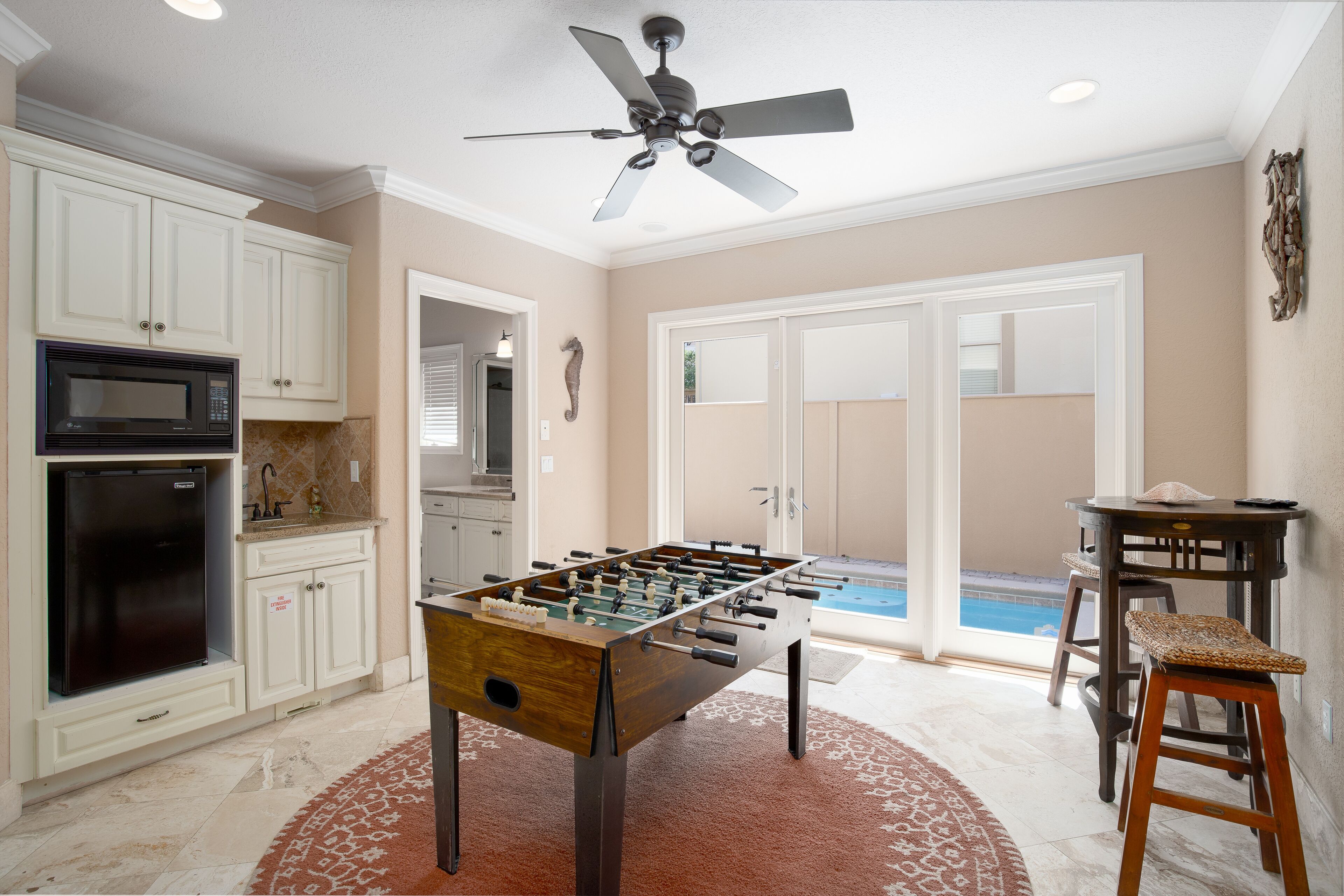 A kitchen with a foosball table, a ceiling fan, and a pool in the background.