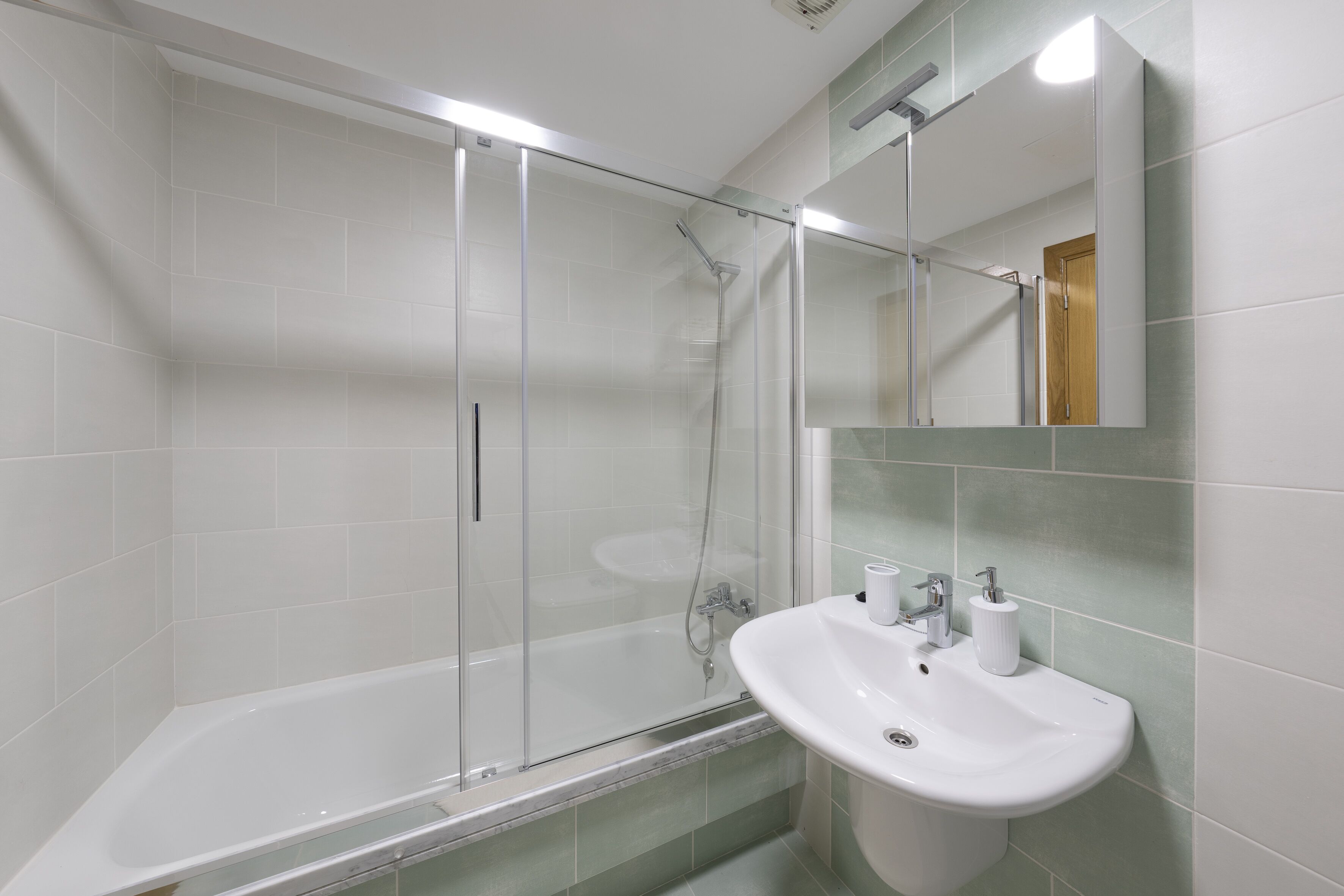 A modern bathroom with a glass-enclosed shower, a white sink, and a mirror above it.