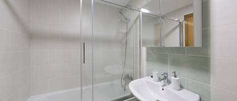 A modern bathroom with a glass-enclosed shower, a white sink, and a mirror above it.