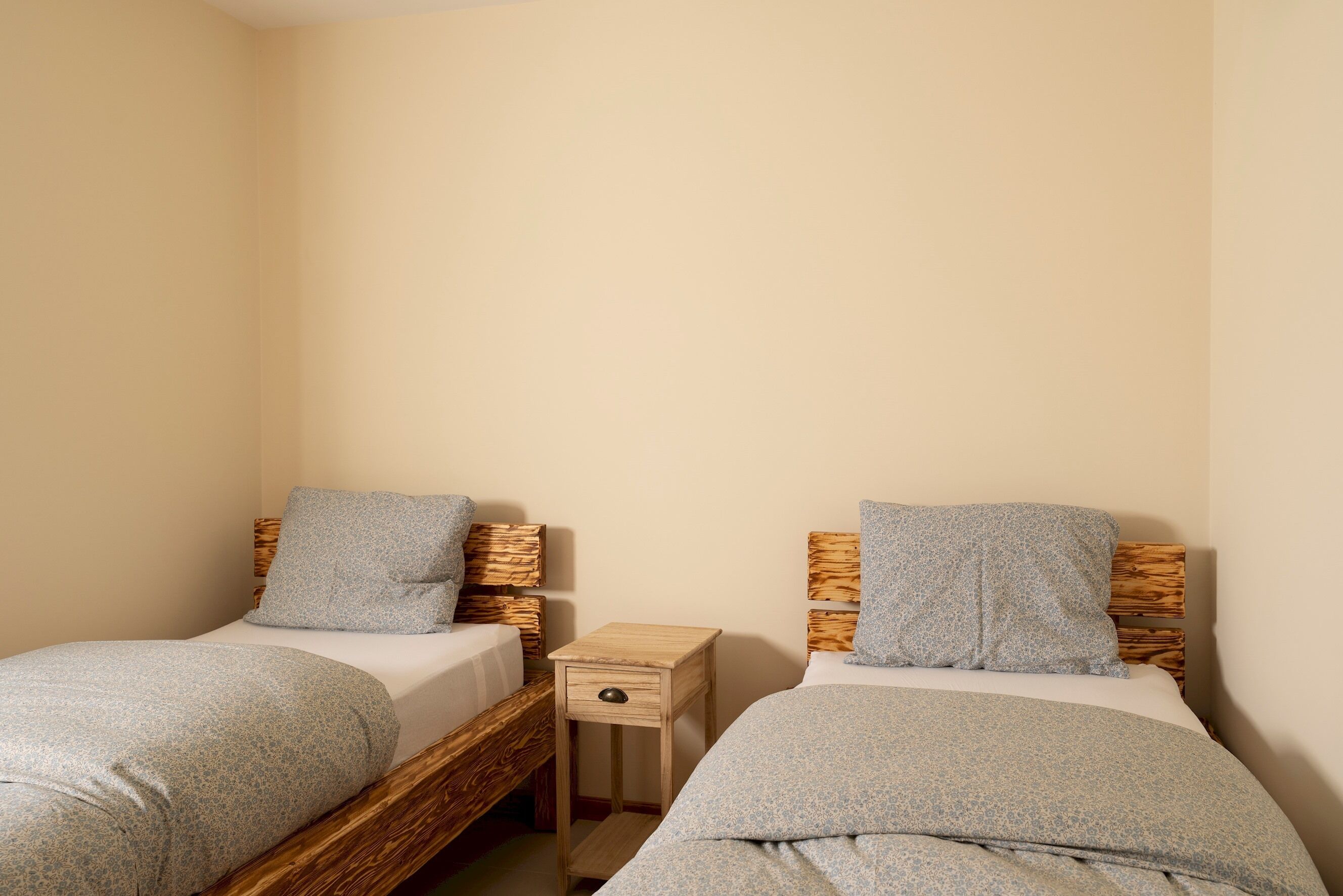 A small, cozy bedroom with two single beds, each with a wooden headboard and matching pillows.