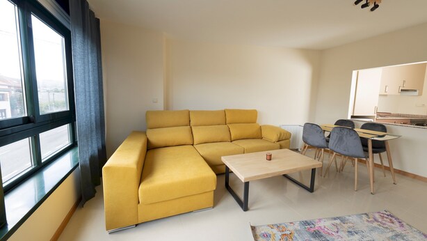 En moderne stue med en gul hjørnesofa, et lille træsofabord og et spiseområde med bord og stole.