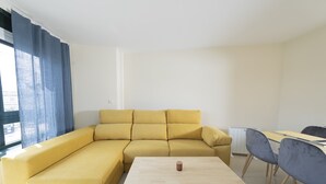 En stue med en gul, modulopbygget sofa, et træsofabord og et spiseområde med et bord og stole.