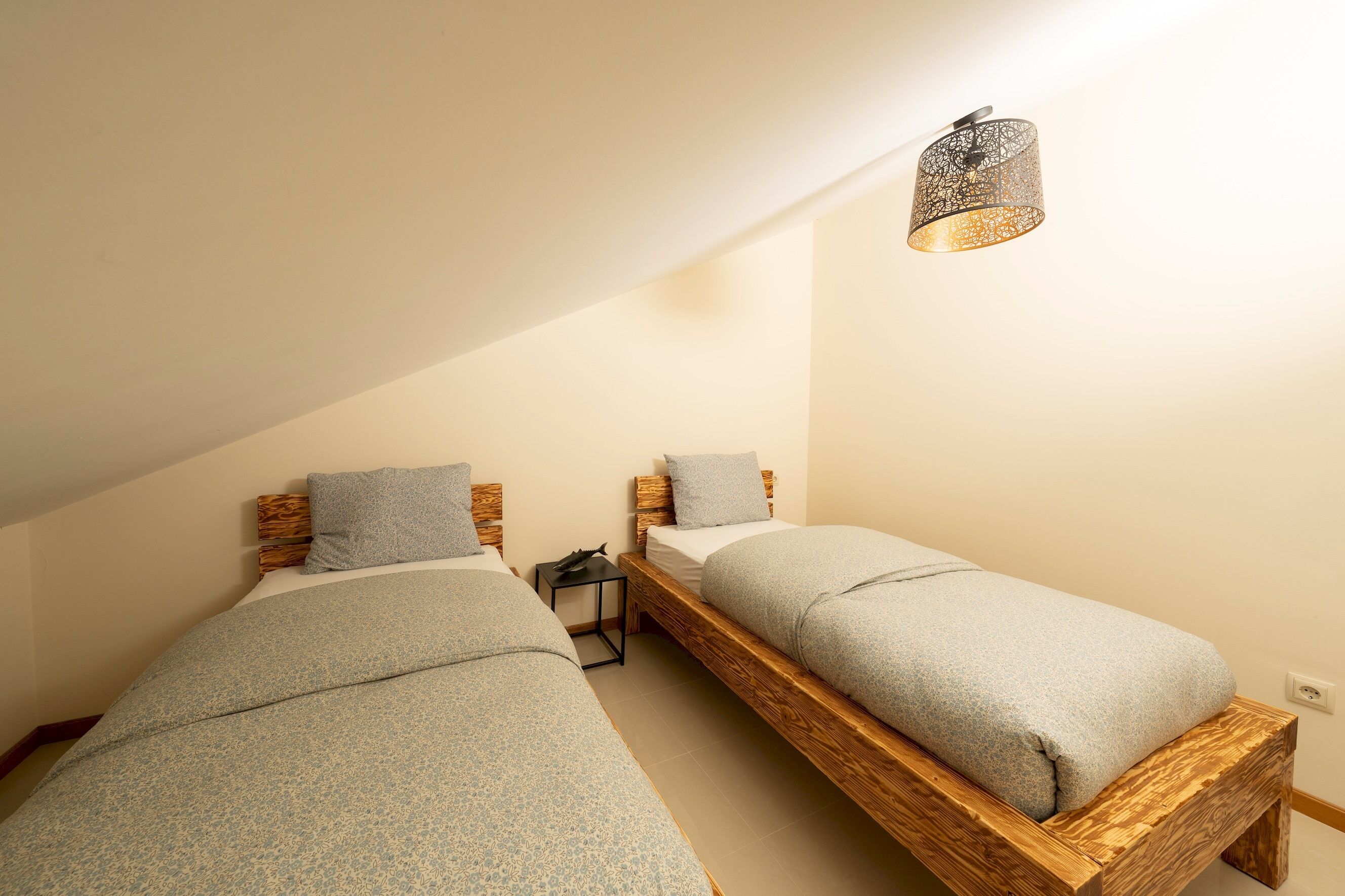 A bedroom with two wooden bunk beds, a small bedside table, and a wall-mounted light fixture.