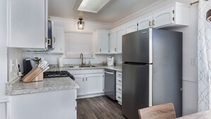 Una cocina moderna con armarios blancos, un refrigerador de acero inoxidable, una estufa a gas y una encimera de madera.
