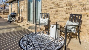 Un patio con dos sillas y un tapete estampado, una parrilla de barbacoa y un calentador de agua junto a una pared de ladrillo.