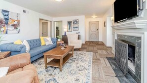 A living room with a blue sofa, a wooden coffee table, a patterned rug, a fireplace, and a television mounted on the wall. - Sunshine Terrace 2BR, perfect for business travel! (Amarillo)