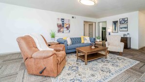 A living room with a brown leather chair, a blue sofa, a wooden coffee table, and a patterned rug. - Sunshine Terrace 2BR, perfect for business travel! (Amarillo)