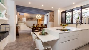 Una cocina moderna con armarios blancos, una isla central y un comedor con una escalera que sube a un nivel superior.
