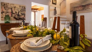Una mesa de comedor dispuesta con platos, vasos y una botella de vino, rodeada de follaje y adornos.