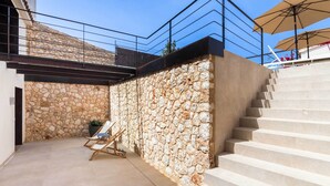Una pared de piedra con una silla de madera y una escalera que conduce a un balcón.