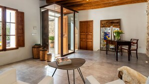 Un amplio salón con techo de madera, un ventanal de vidrio que da al exterior, una mesa de comedor con sillas y un sofá blanco.