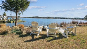 A lakeside view with three Adirondack chairs facing the water, a dock with boats, and a tree in the foreground. - Short drive to Downtown Cambridge | Private Dock | Guest House | Pool | Hot Tub (Cambridge)