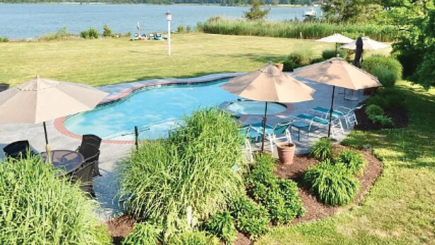 A swimming pool with lounge chairs and umbrellas, surrounded by a grassy area with a view of a lake and trees. - Short drive to Downtown Cambridge | Private Dock | Guest House | Pool | Hot Tub (Cambridge)