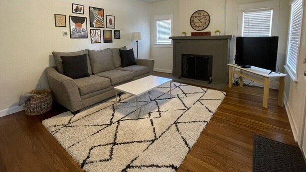 A living room with a sofa, a coffee table, a fireplace, a TV on a stand, and framed artwork on the wall. - Urban Hideaway - Cozy & Remodeled 2 BR! (Amarillo)