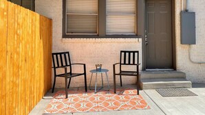 A small patio area with two chairs and a table, a wooden fence, and a door with a window above it. - Urban Hideaway - Cozy & Remodeled 2 BR! (Amarillo)